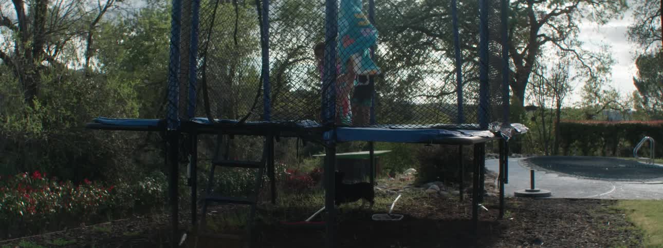 Two girls and a boy jump on a trampoline causing a dog underneath to freak out