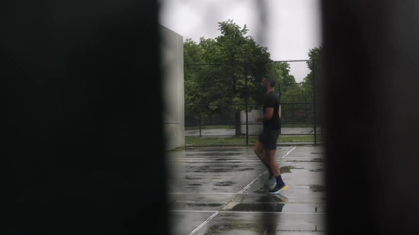 A person is doing cardio on a wet court behind a chainlink fence