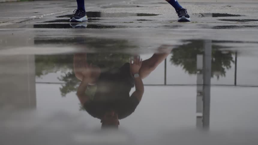 Reflection of a man stretching seen from a puddle of water on the sidewalk