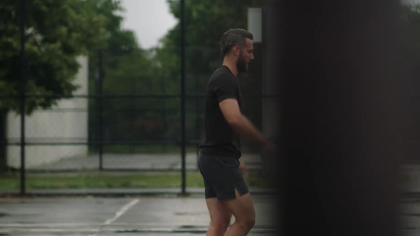 A man performs stretches on a tennis court on a rainy day
