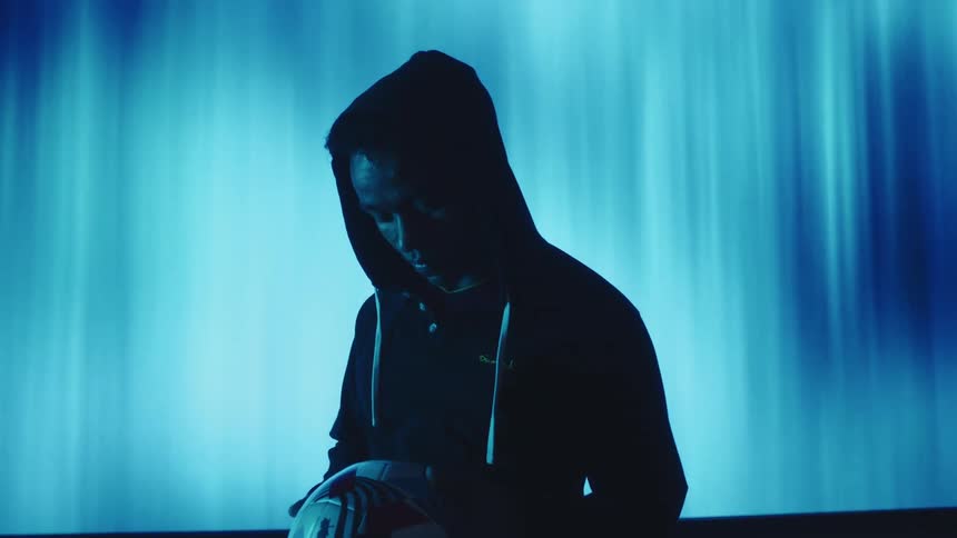 Silhouette of a man in a hoodie indoors in low lighting holding a ball in his hands