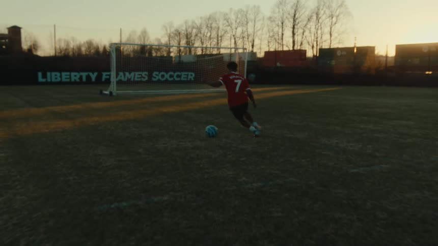 A person is playing football on a football field and is dribbling the ball close to the goal