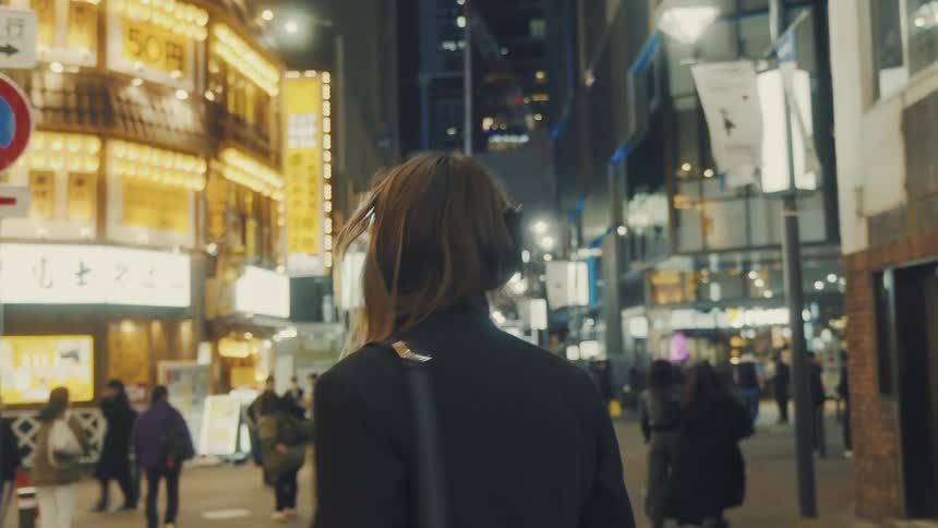 Young woman walking down a street with many pedestrians at night in a metropolis