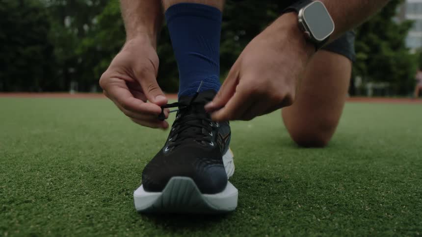 An athlete ties his shoe while kneeling on a sports field
