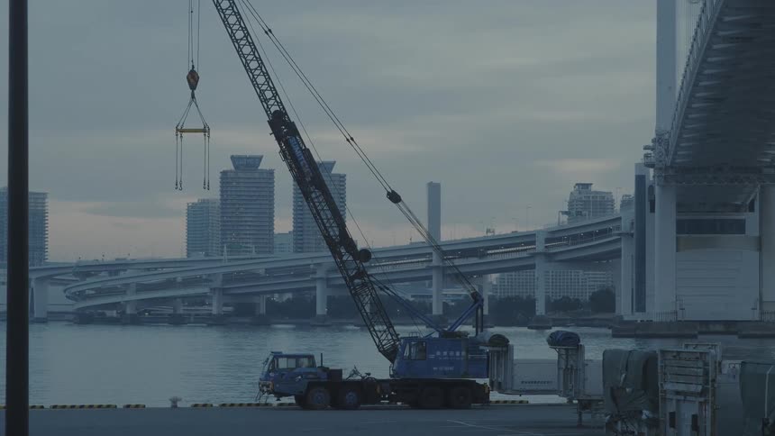 A crane on a truck sits by a river running through a large city
