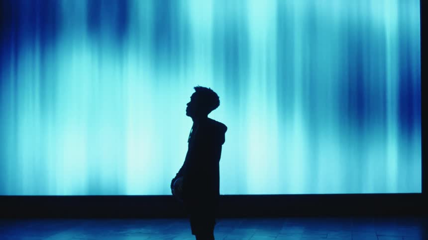 A silhouette of a person who is standing still and behind there is a blue neon light