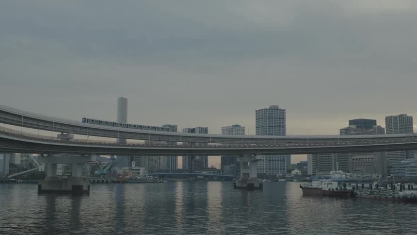 A bridge like a train passing over a bay of water with some boats standing at the docks