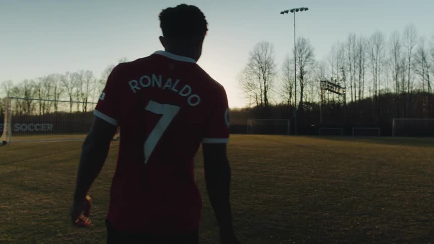 A man in a red uniform is turning his back and walking on a football field