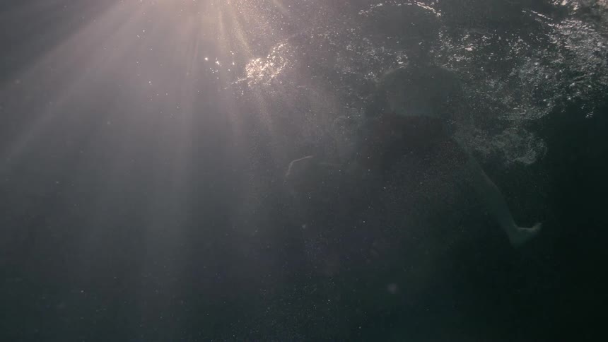 Man swimming towards a sunlight on the surface of the ocean