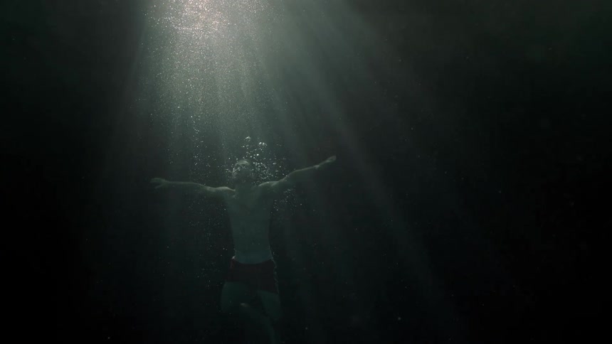 Man submerged in dark water reaching for a beam of light from above