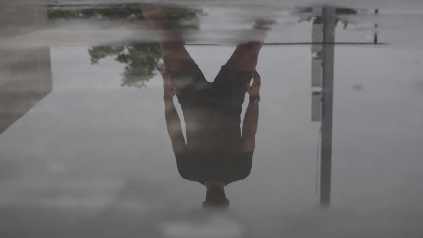 Reflection in a puddle of a man stretching his body before workout