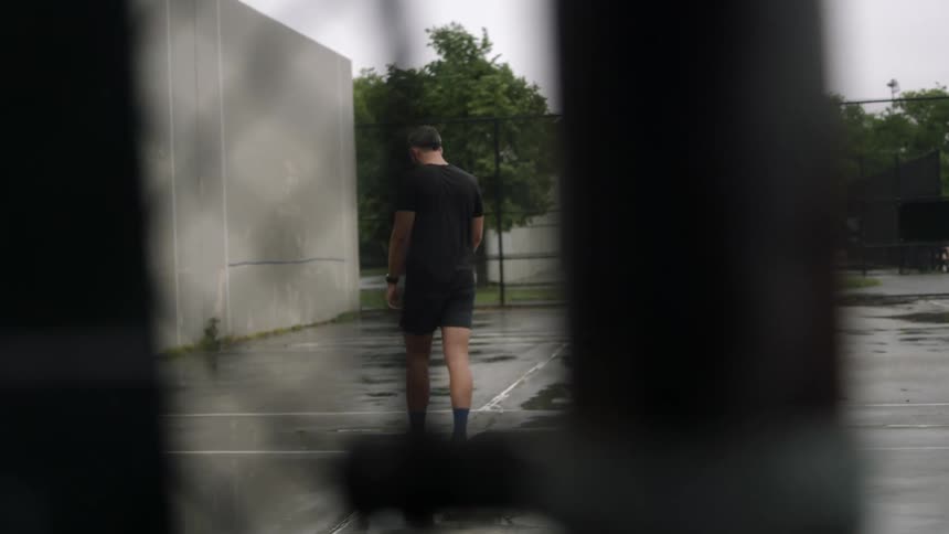 A man walks around a tennis court on a rainy day