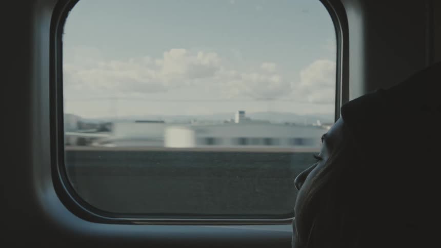 A young female stares out of a train window as it moves through a city
