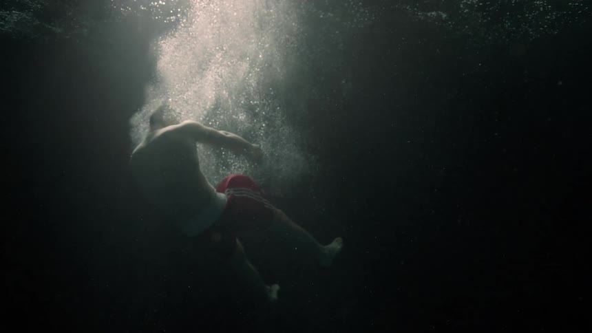Man submerged in dark water illuminated only by the light that penetrates the waters surface