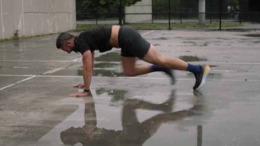 A man performs stretching and cardio exercises on a wet outdoor court