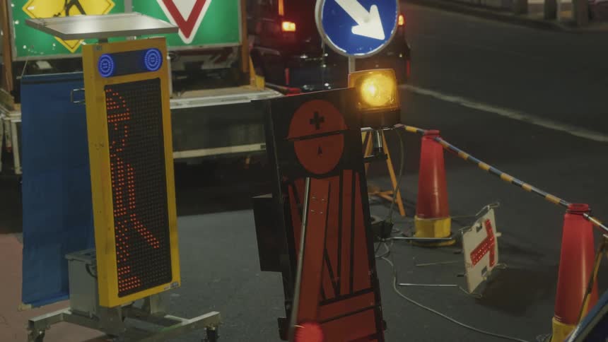 Night scene of a street with temporary construction signs including cones signs and an electronic panel with an arrow indicating the permitted direction for vehicles
