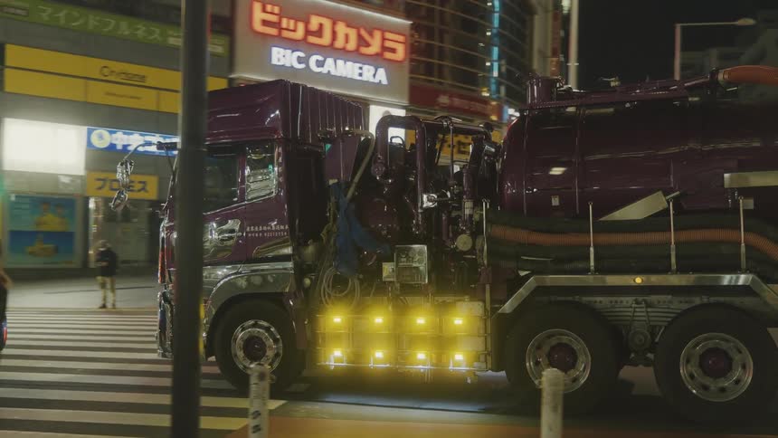 A large truck with a tank rolls through a city intersection at night