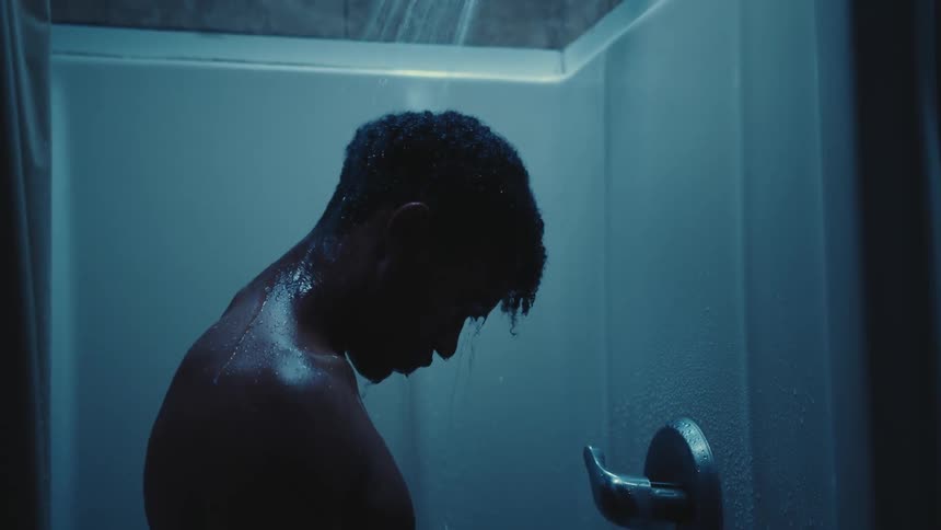 A young man takes a shower looking down at the floor
