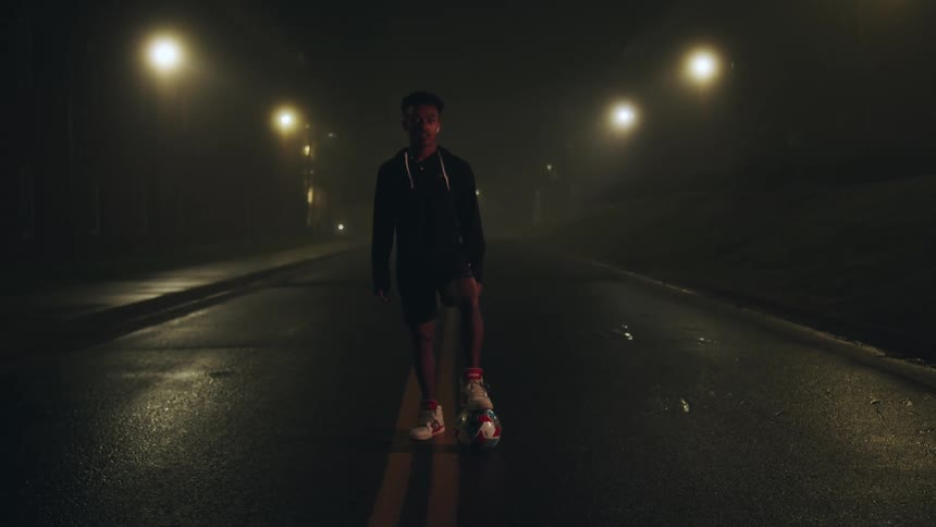Boy in the middle of a wet street at night with a soccer ball on his foot