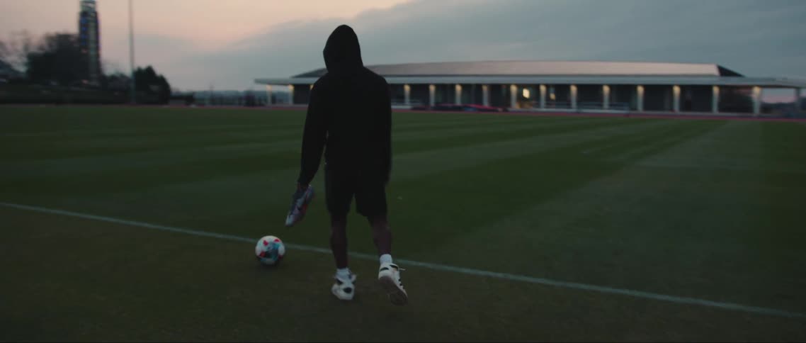 A black athlete walks onto a soccer field and kicks a ball