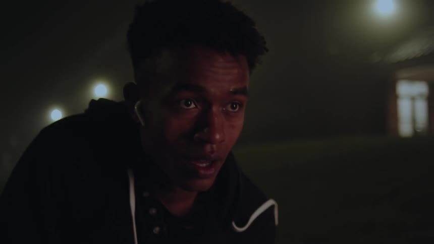 A young black man breathes hard while outside a building at night