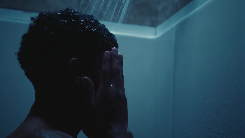 A black man looks sad after rubbing his head and face in the shower