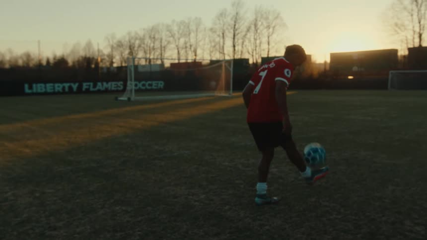 A teenage boy is practicing soccer alone on a soccer field at dusk
