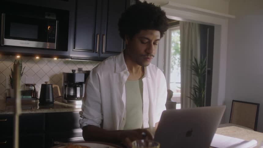 Man sitting in the kitchen typing on a laptop