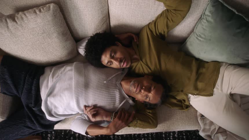 A couple lying on a couch one resting their head on the others chest