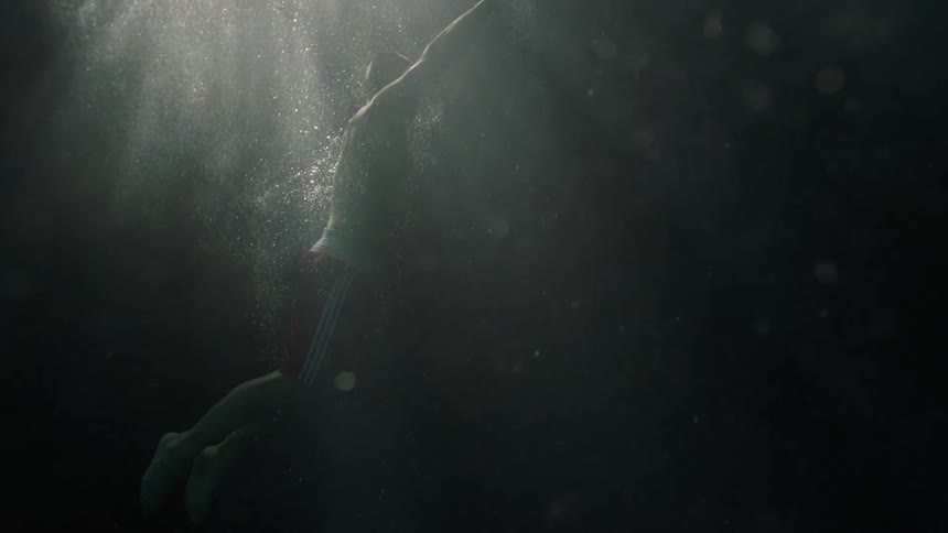 A man swims up through the dark water