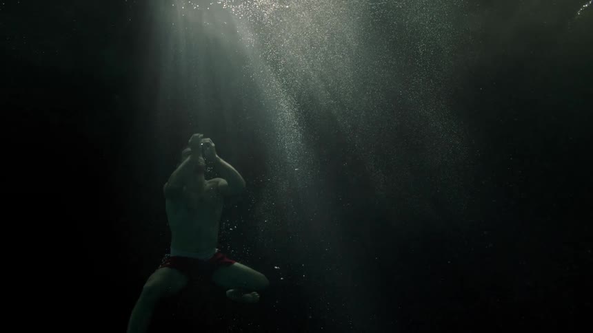 A white male swims through dark water to get to the surface