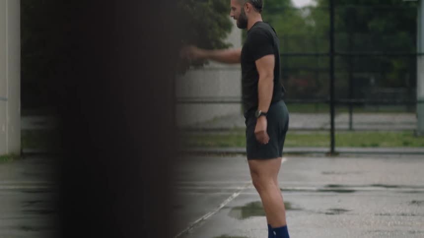 Man performs leg and arm stretches while standing on a wet sports court