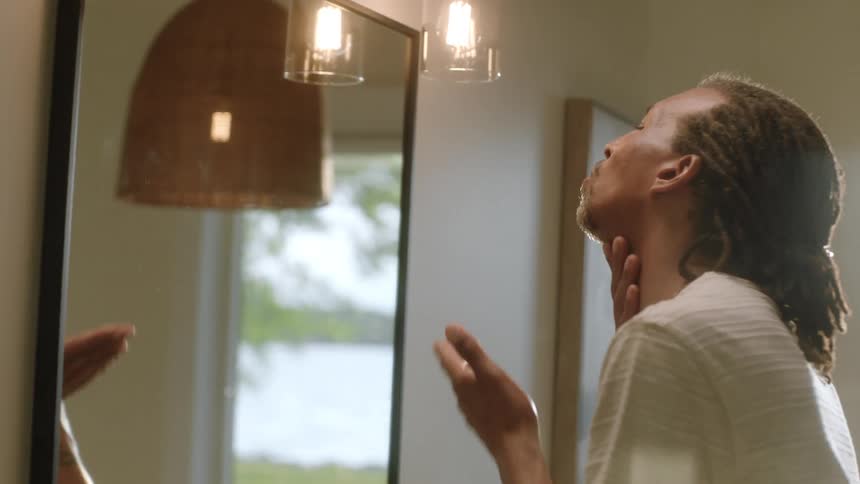 Man in front of the mirror passing his hands over his face and neck