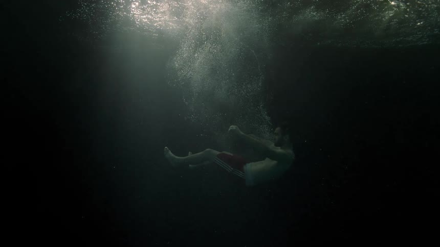 A man jumps into the water sinking slowly to the bottom