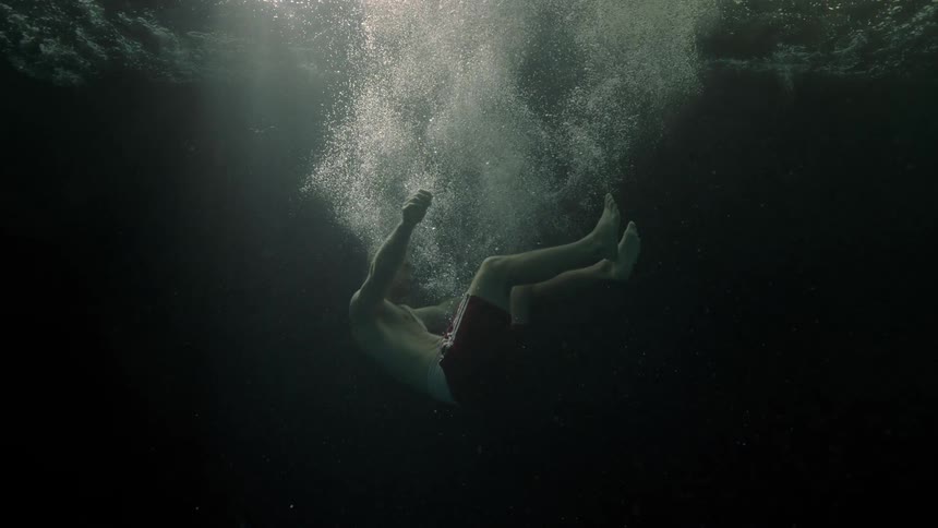A shirtless man splashed into dark water and slowly sinks to the bottom
