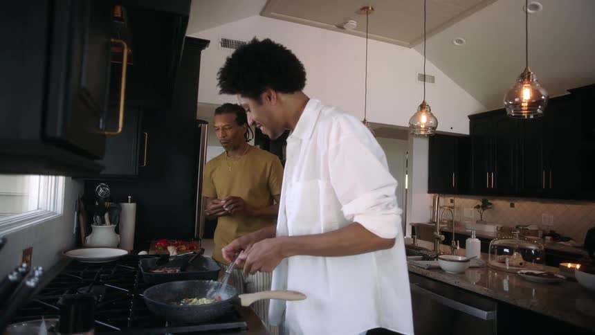 Two smiling men in the kitchen preparing food in a frying pan