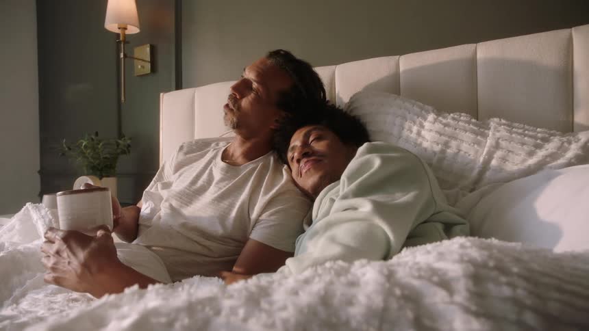 A couple sit in bed together with coffee