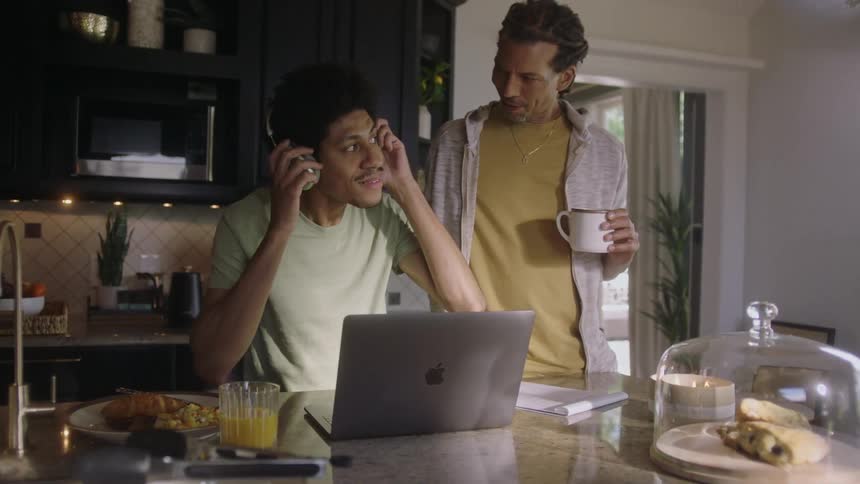 Two black men converse over a laptop and food in a kitchen