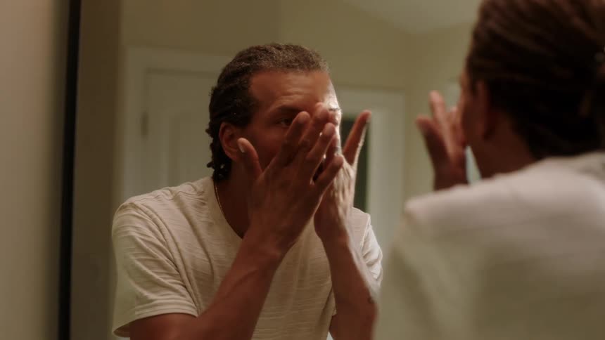 A black man grooms himself while looking in a mirror