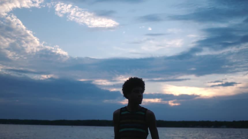 Silhouette of an individual standing by a body of water during sunset or sunrise