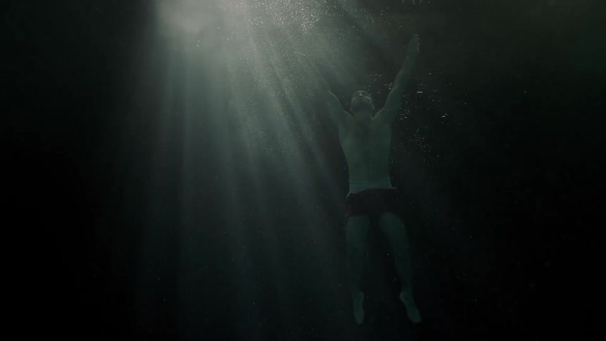 A man swims slowly up from beneath deep water