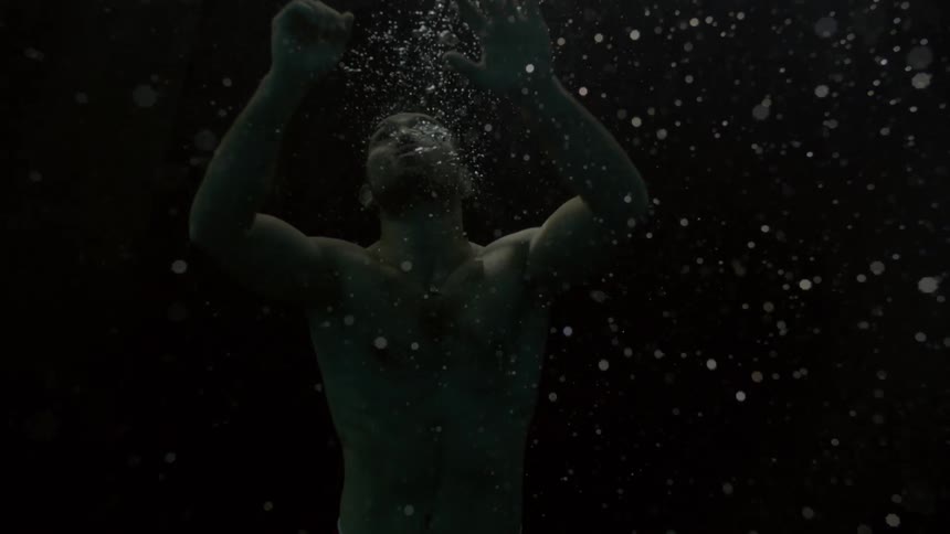 Silhouette of a man submerged in water with bubbles rising around him