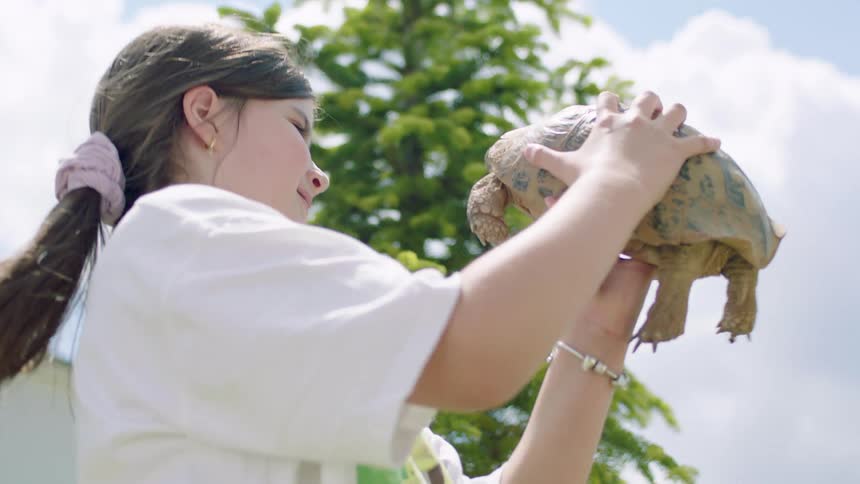 Girl holds a turtle up near her face while turning around in a circle