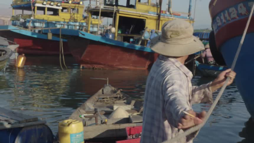 Man in a hat pulling a rope from a boat that is moored at sea