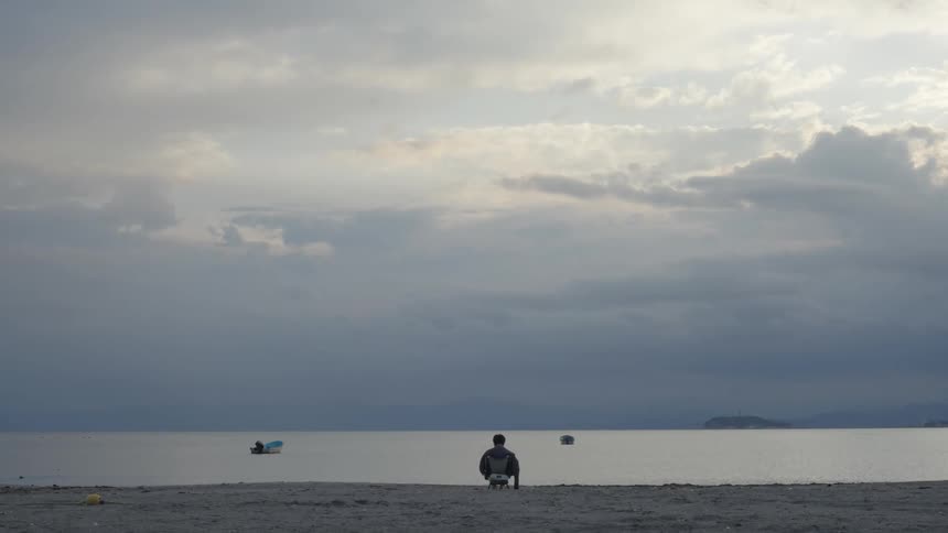 A person sits on a beach and looks out to sea