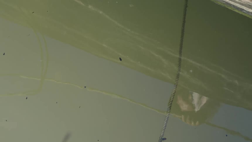 Rope cuts across reflection of person in the murky water