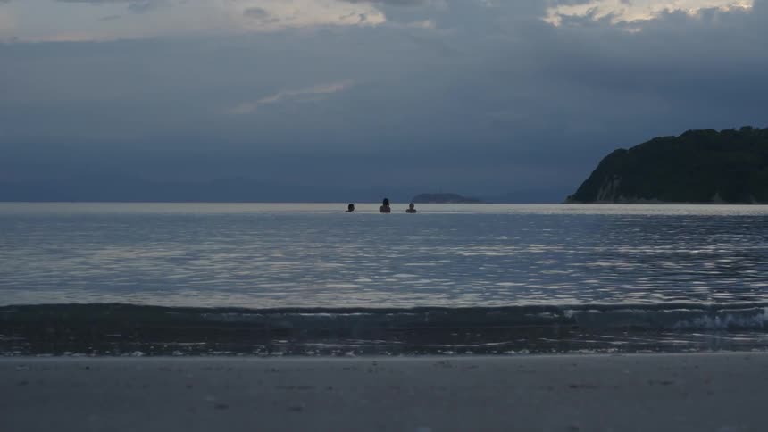 Landscape of a calm beach with three people swimming in the background