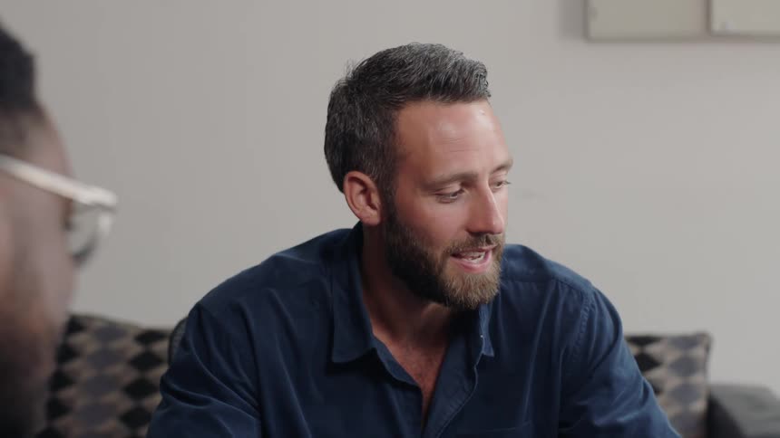 A man sitting a a desk talking to coworkers or clients in an office space