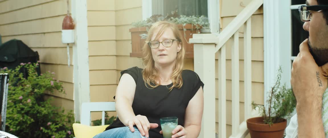 A woman holding a drink converses with a man outside of a home