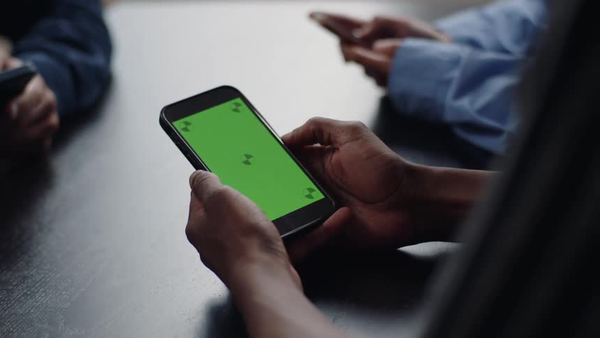 Closeup of peoples hands using a cell phone on a table